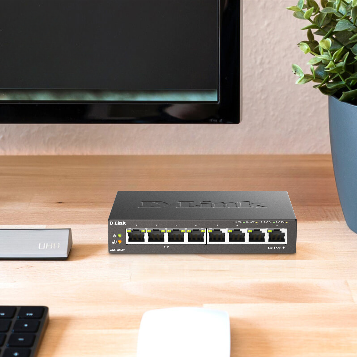 D-Link network switch on a desk with a computer monitor and plant in the background